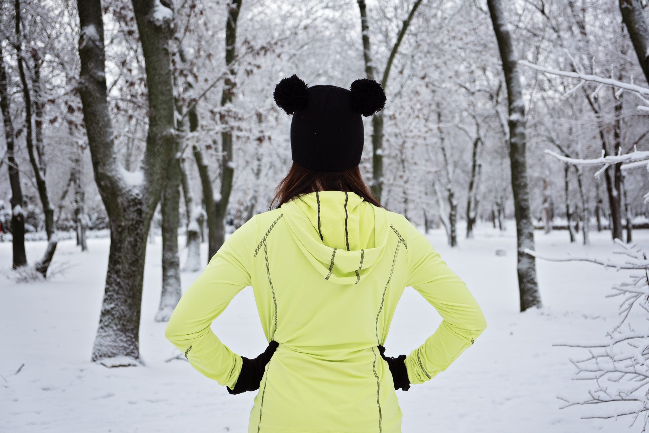 Back view of Woman ready to winter workout outdoor exercise in snowy winter park. Winter fitness, exercising in cold weather. Sportswoman go to outdoor exercising in nature at snowy winter park